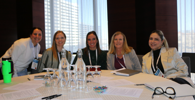 A group of people in suits sit around a table filled with papers and water glasses