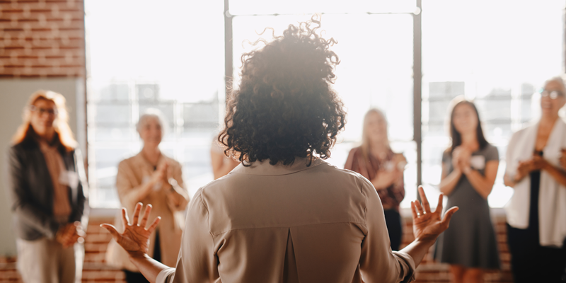 A person with curly hair stands in front of a group of feminine individuals