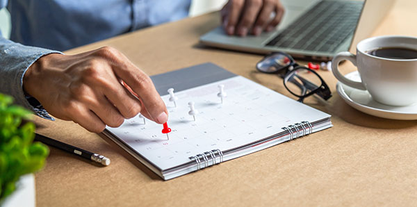 A hand places a red pushpin on a calendar