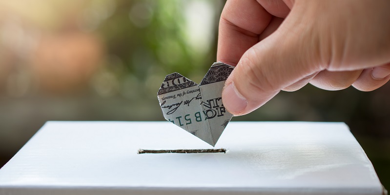 A hand places a small dollar bill folded into a heart in a white box